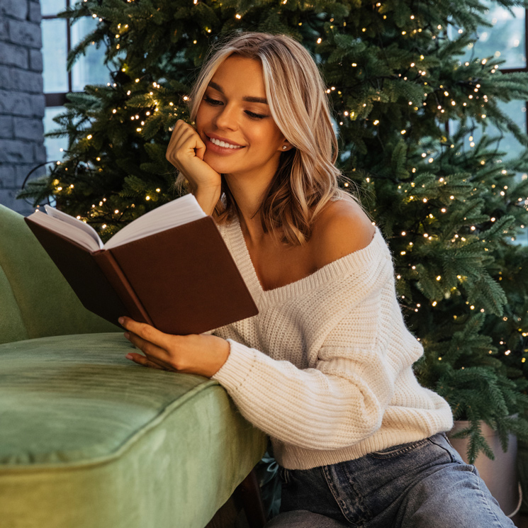 Mujer leyendo un libro junto al árbol de Navidad